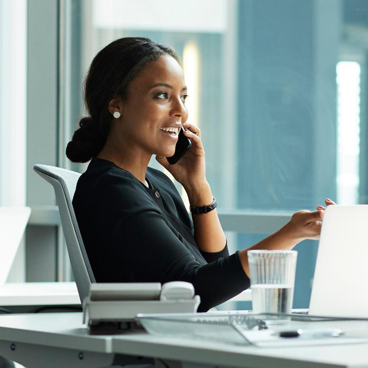 A cheerful businesswoman is working proficiently on her laptop at her office desk.