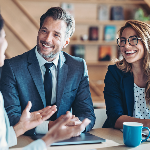 A businessman and businesswoman are seated in an office, engaging in a professional meeting with a group of colleagues.